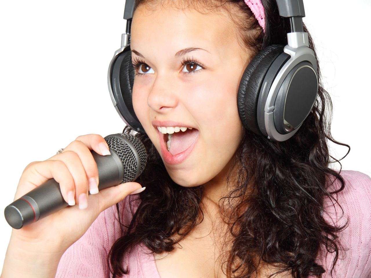 A young woman passionately singing with headphones and microphone on a white background.