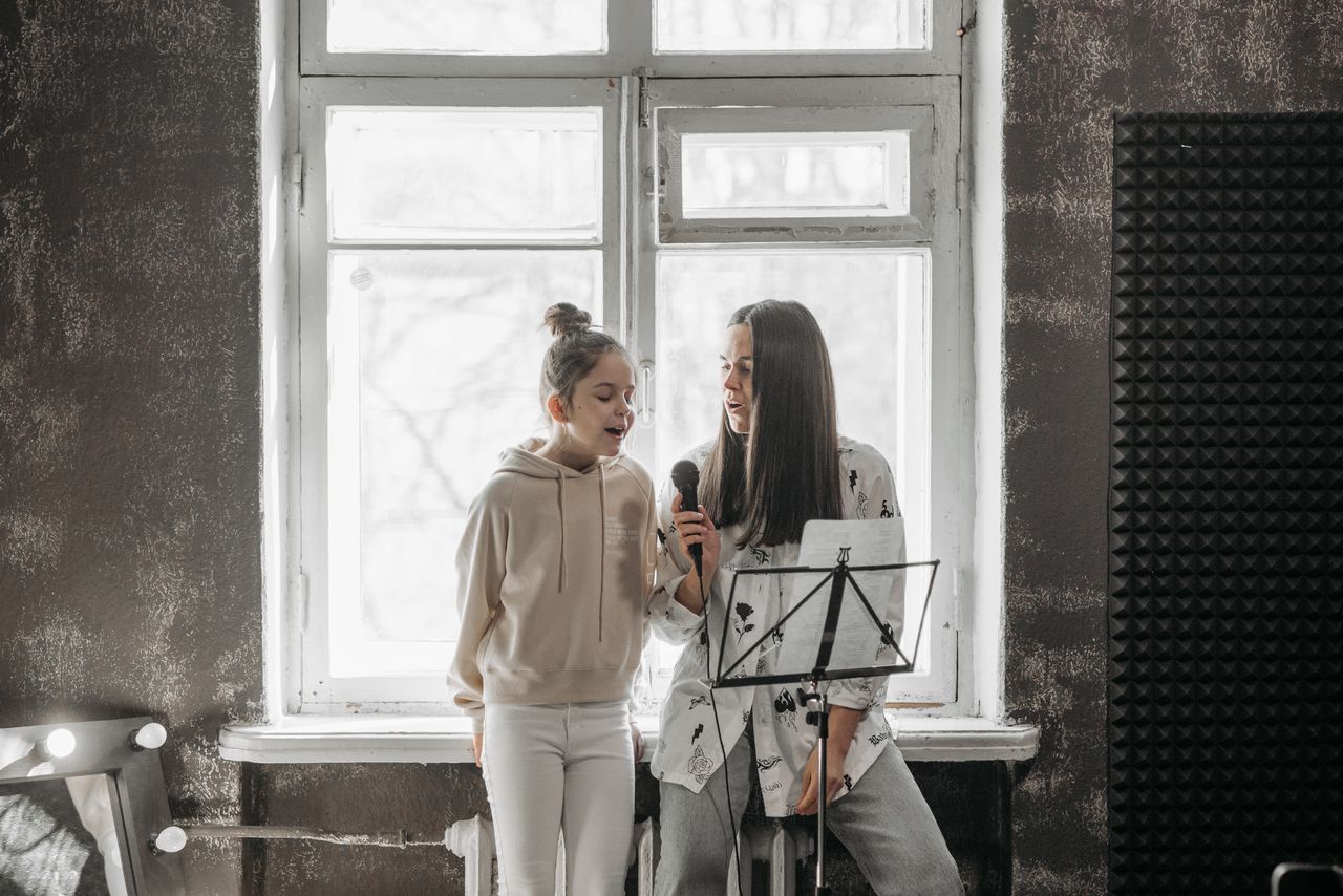 A young girl and her teacher practicing singing in a music studio.